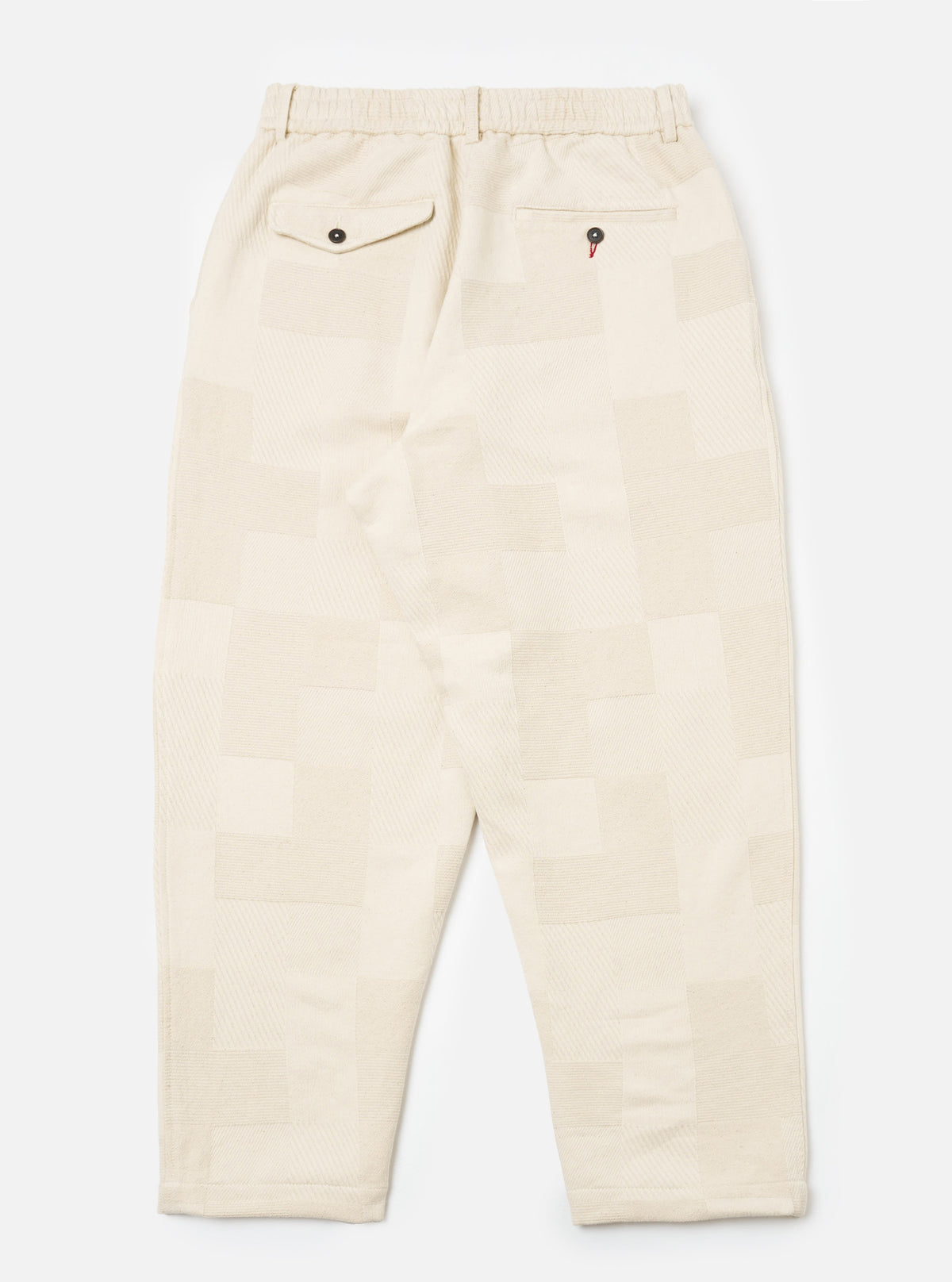 Back view of Ecru Patchwork Weave Cotton Pleated Track Pant on a white background. The pants have a relaxed fit and feature a unique patchwork design.