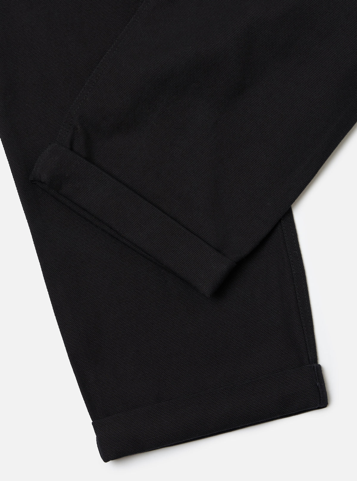 Close-up of the Black Organic Canvas Super Chino pants. The black canvas material is cuffed at the bottom. Shot on a white background.
