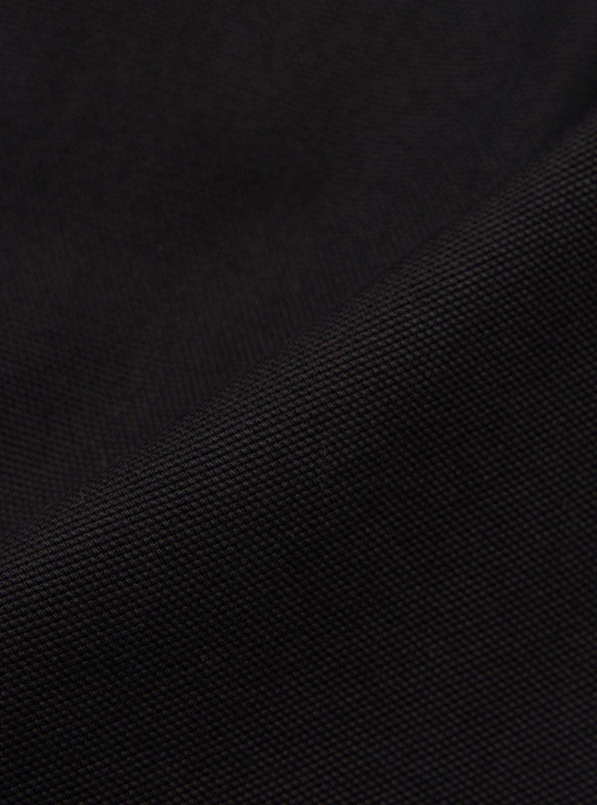 Close-up of the Black Organic Canvas Super Chino fabric. The dark canvas material is textured and folded against a plain background.