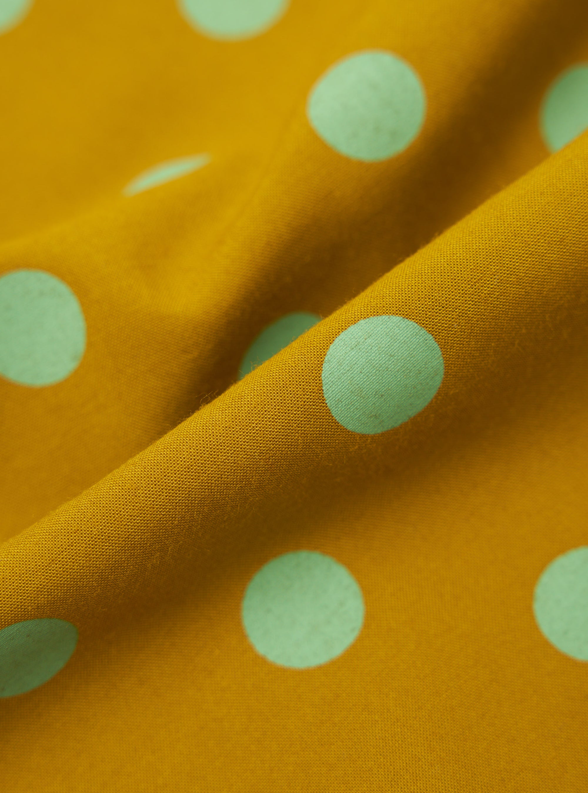 Close-up of the Mustard Bold Dot Print Rayon Evening Scarf. The scarf is mustard yellow with light green polka dots. The rayon fabric is draped to show texture.
