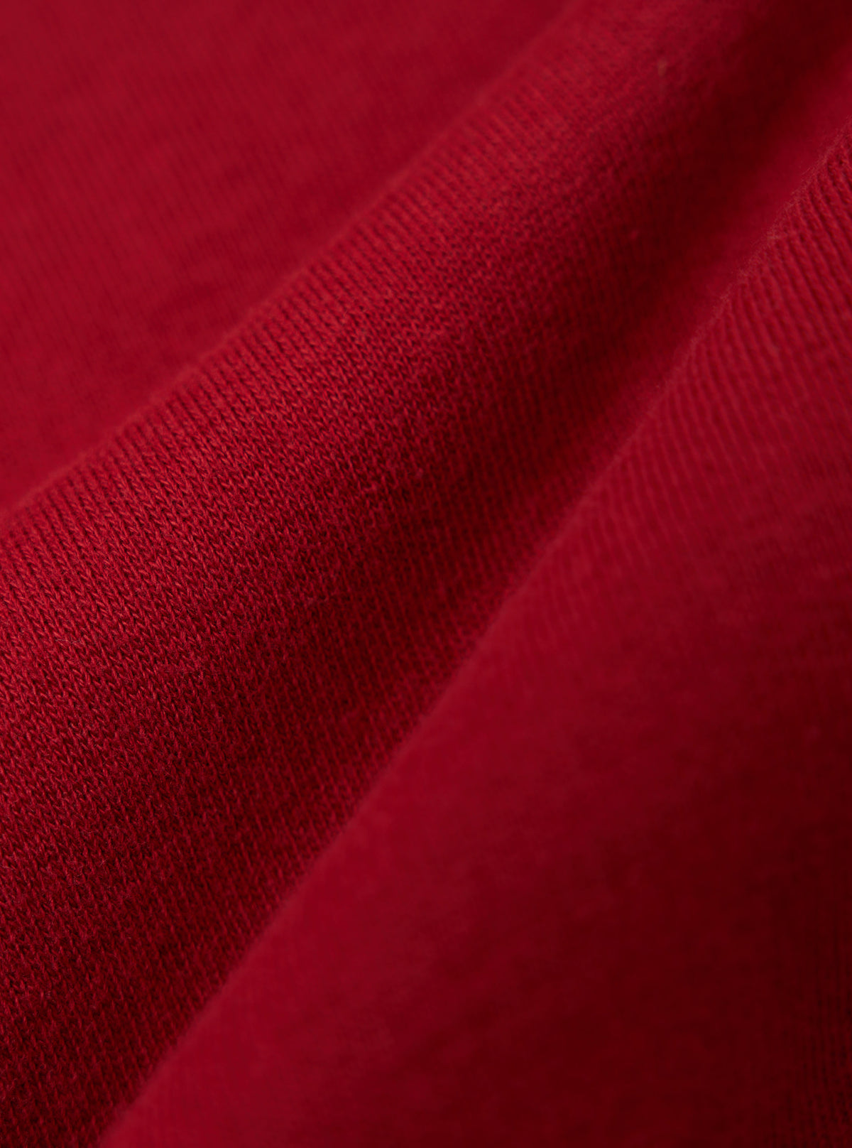 Close-up of the red fabric of the Red Brush Back Sweat Tyler Sweat Jacket, showing the texture and color. The jacket is casually draped on a flat surface.