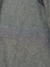 Close-up of the Charcoal Organic Chambray Patched Lazy Day Shirt, showing the fabric texture and patched pocket detail. The shirt is laid flat on a neutral surface.