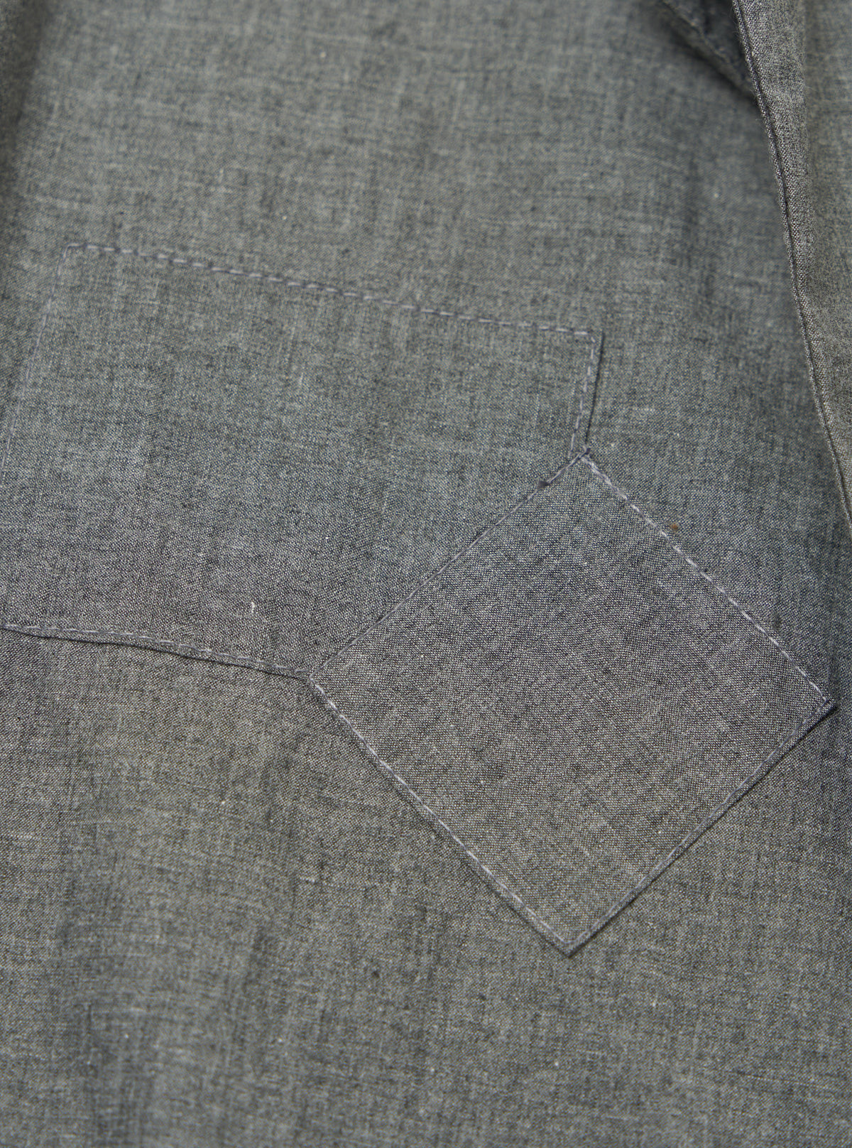 Close-up of the Charcoal Organic Chambray Patched Lazy Day Shirt, showing the fabric texture and patched pocket detail. The shirt is laid flat on a neutral surface.