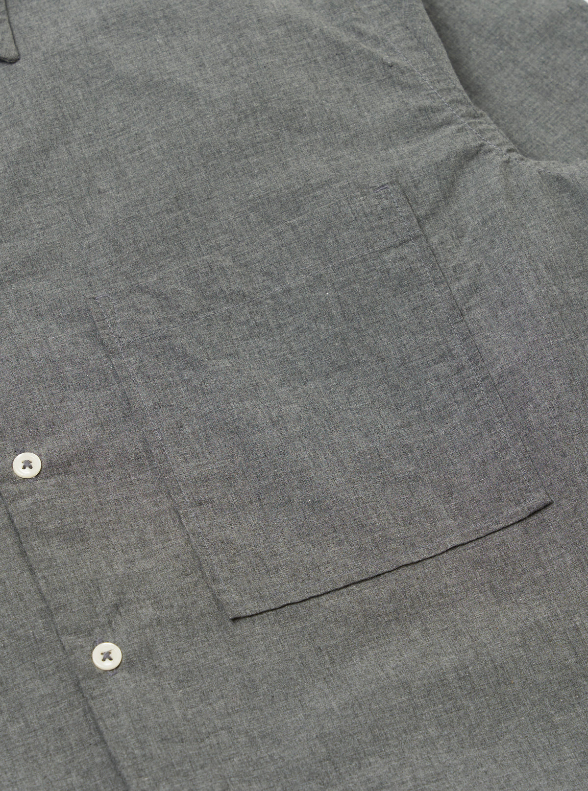 Close-up of the Charcoal Organic Chambray Lucky Shirt, showing the fabric texture, pocket, and buttons. The shirt is laid flat on a neutral surface.