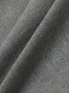 Close-up of the Charcoal Organic Chambray Lucky Shirt fabric. The soft, textured material is folded on a plain surface, highlighting its weave and color.