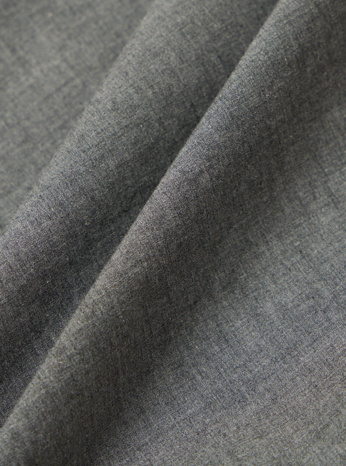 Close-up of the Charcoal Organic Chambray Lucky Shirt fabric. The soft, textured material is folded on a plain surface, highlighting its weave and color.