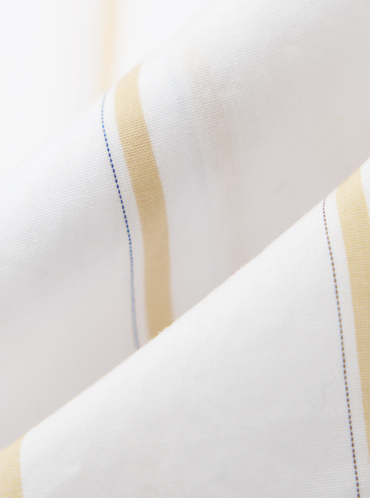 Close-up of the White Office Stripe Square Pocket Shirt fabric. Features white material with gold and blue stripes. The shirt is folded on a white surface.