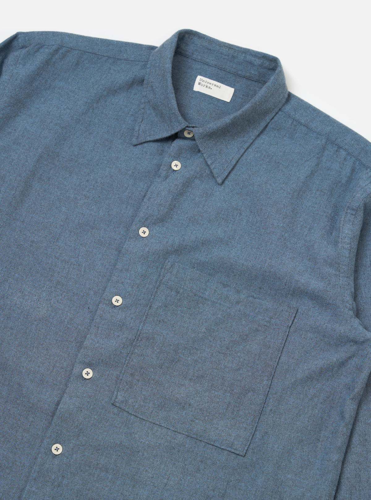 Close-up of the Blue Brushed Marl Twill Square Pocket Shirt on a white background. The shirt is blue with a square pocket and white buttons.