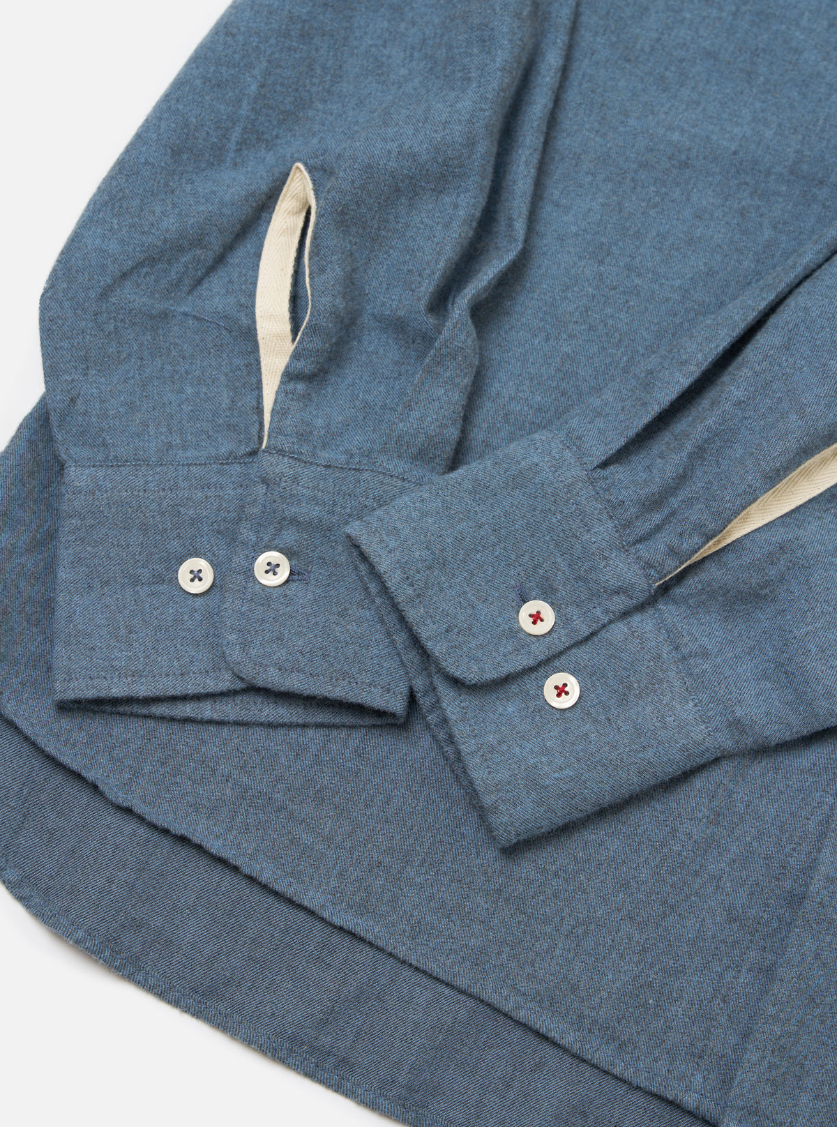 Close-up of the Blue Brushed Marl Twill Square Pocket Shirt on a white surface. Shows the blue twill fabric, buttoned cuffs, and contrasting trim.