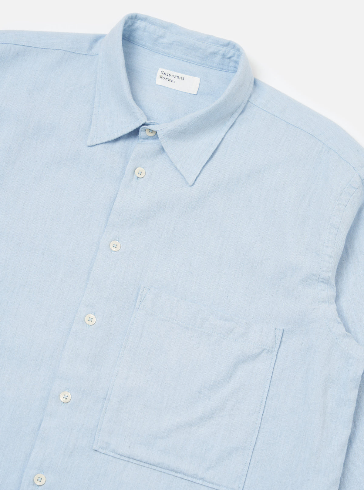 Close-up of the Light Blue Brushed Marl Twill Square Pocket Shirt on a white surface. The light blue shirt features a square pocket and white buttons.