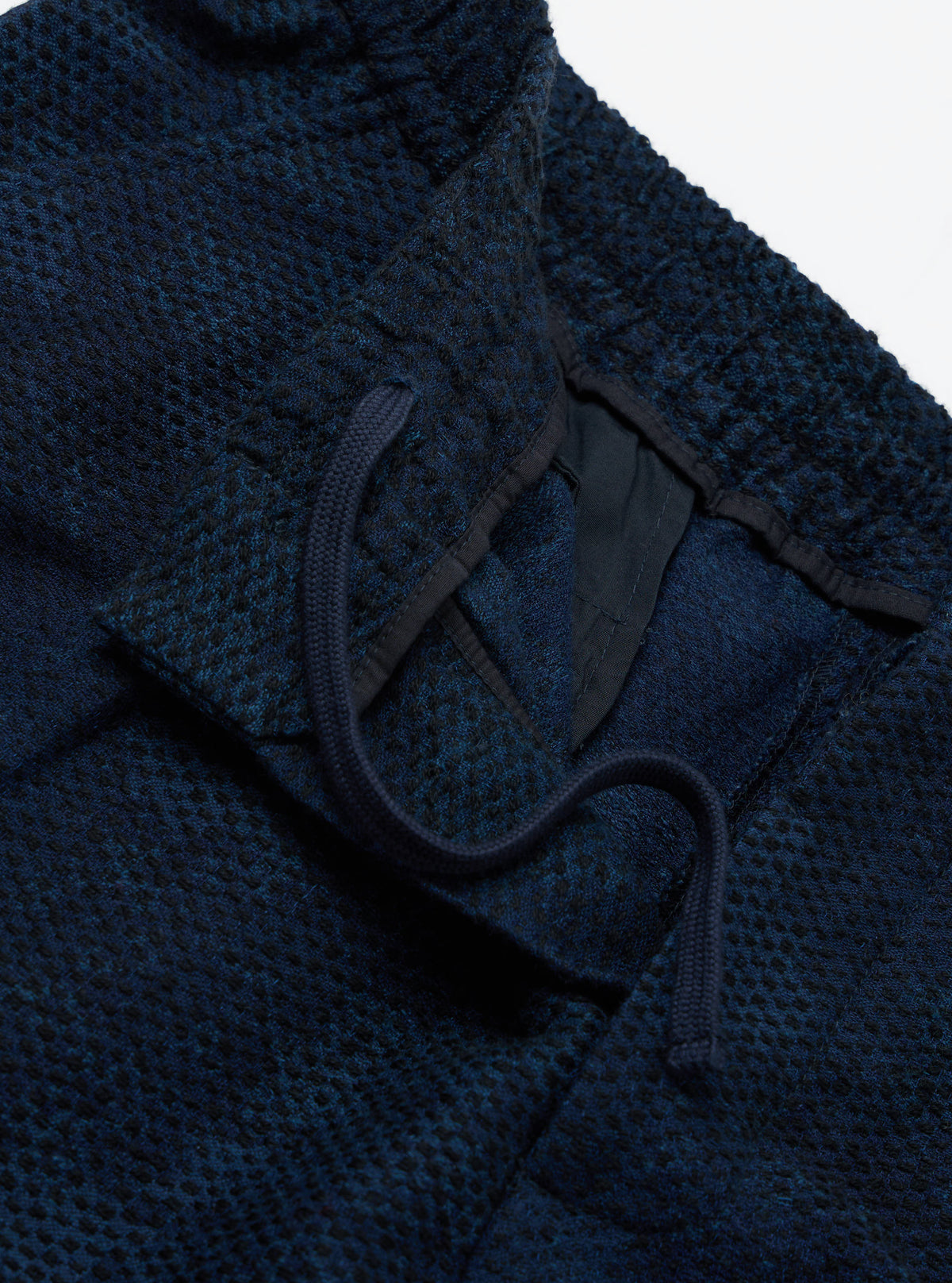 Close-up of the Black/Indigo Denim Camo Pleated Track Pant on a white surface. The denim shows a subtle camo pattern. Drawstrings are visible at the waist.