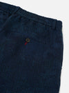 Close-up of Black/Indigo Denim Camo Pleated Track Pant on a white surface. The denim has a subtle camo pattern. Features a buttoned pocket with red stitching detail.