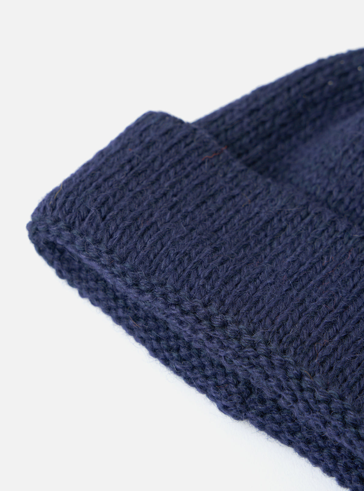 Close up of the Navy Alpaca/British Wool Bobble Hat showing the texture of the knit on a white background.