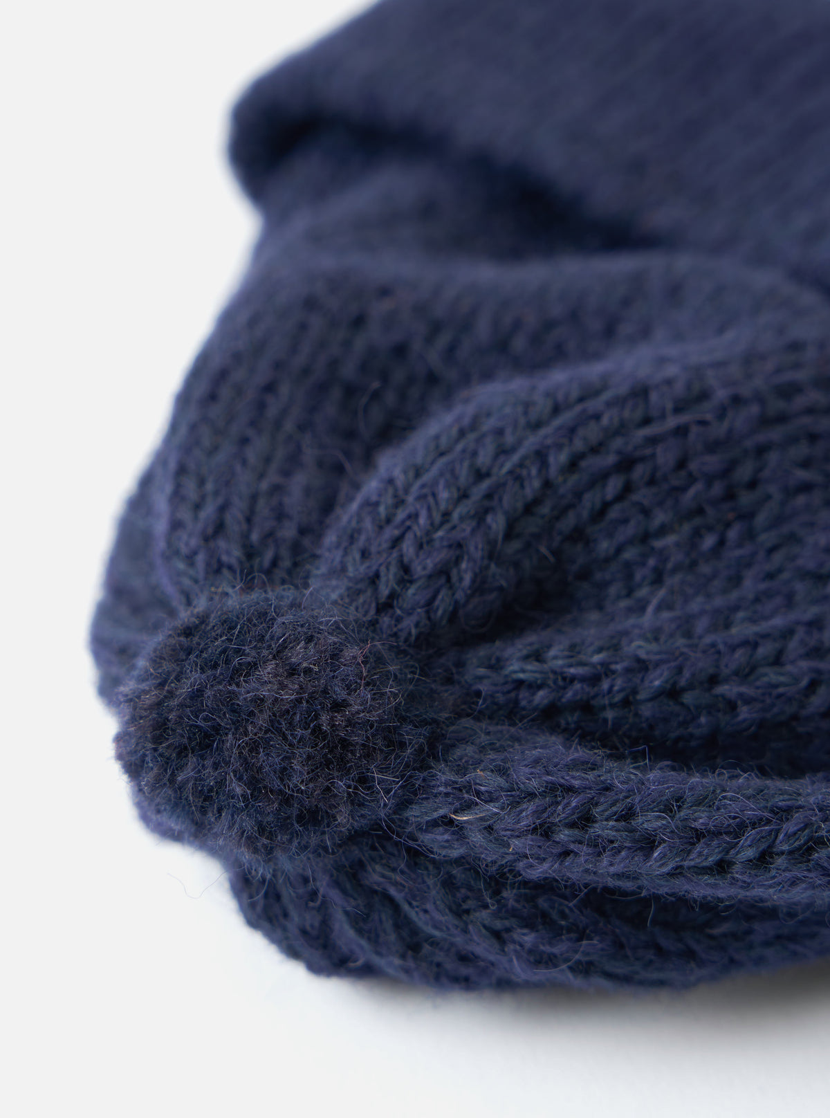 Close-up of a navy Alpaca/British Wool Bobble Hat on a white background. The knit is clearly visible, showing the texture of the wool and alpaca blend.