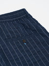 The Navy Chester Stripe Pleated Track Short is shown from a rear perspective, laid flat against a plain white background. The image highlights the two rear pockets, one of which is a buttoned jetted pocket, and the elasticated waistband. The fabric features a dark navy and white pinstriped seersucker texture.