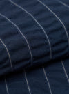 A detailed, close-up fabric swatch of the Navy Chester Stripe Pleated Track Short reveals a pattern of thin, vertical white stripes on a dark navy blue cotton base. The image focuses on the fine texture and weave of the material.