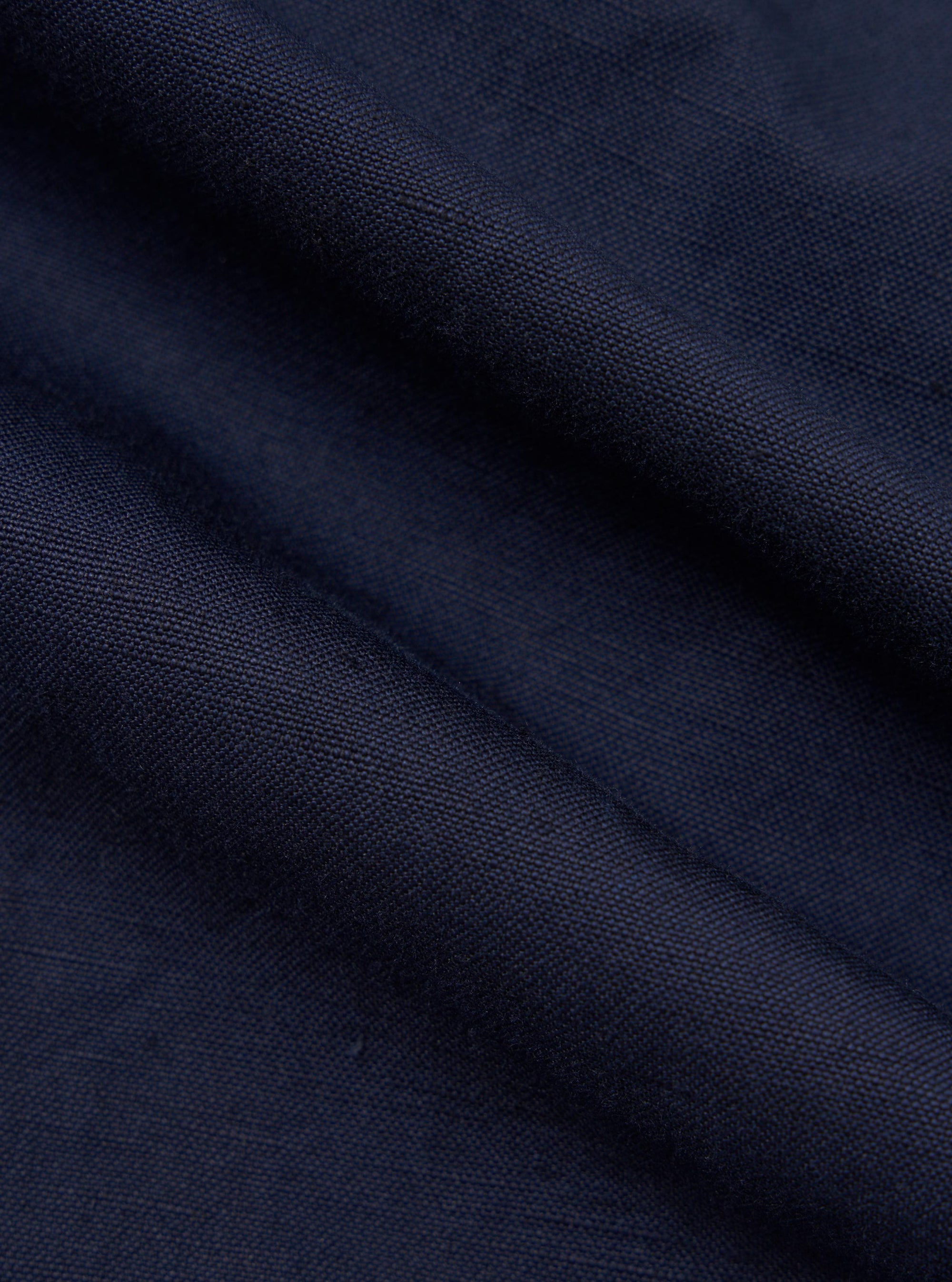 A close-up fabric swatch of the Navy Linen Slub Weave Franck Jacket highlights the deep navy blue color and the intricate, irregular texture of the slubbed linen-cotton blend. The image provides a detailed view of the fabric's tactile quality and woven appearance.