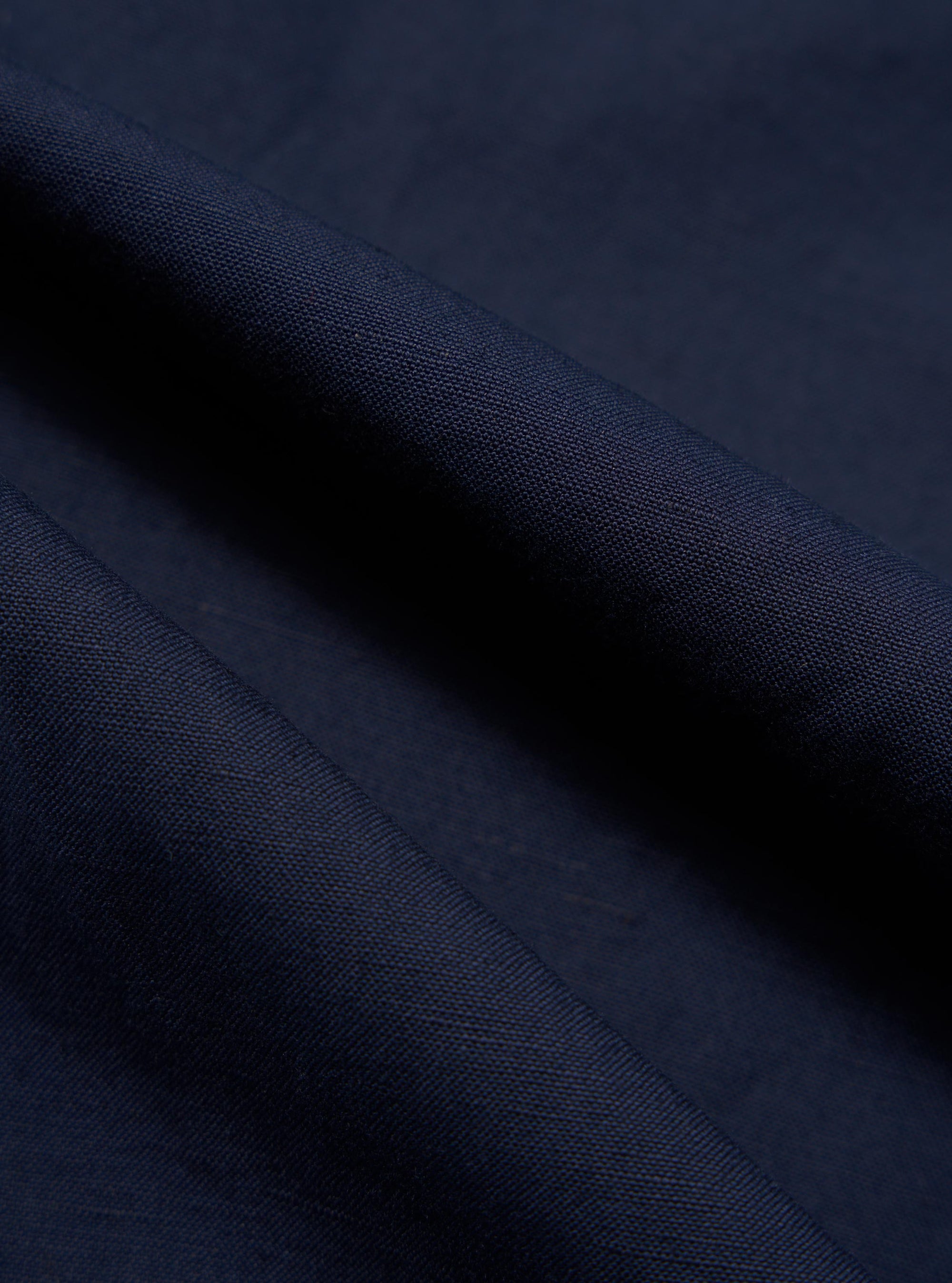 A close-up, square fabric swatch of the Navy Linen Slub Weave Dizzy Trouser highlights the material's deep navy blue color and intricate texture. The image shows a visible weave with characteristic irregular slubbed yarns, creating a subtle, natural variation across the surface of the cotton-linen blend.