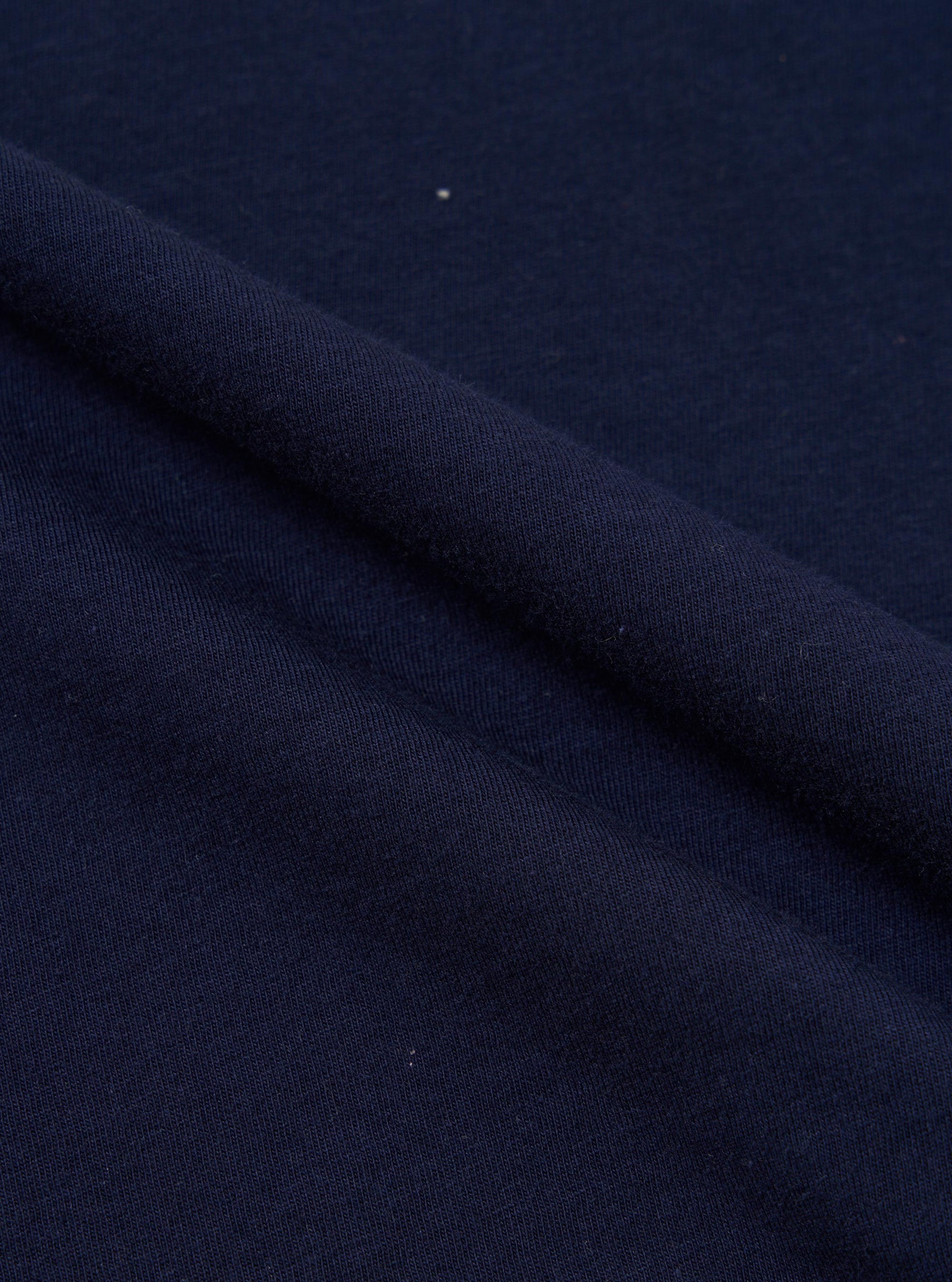 A close-up fabric swatch of the Navy Single Jersey Multi UW Print Multi UW Print Tee shows a detailed view of the navy blue cotton material. The image highlights the single jersey knit texture and the repeating multi-colored UW logo print across the surface.