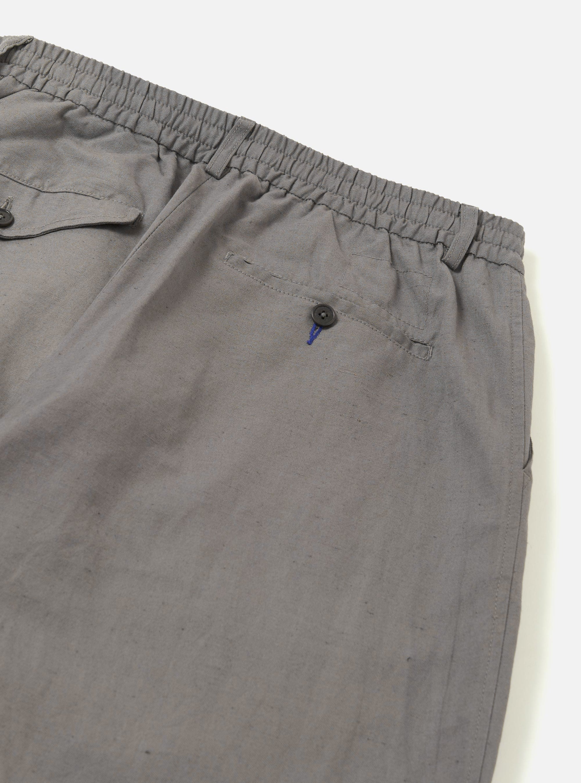 The Mid Grey Linen Slub Weave Oxford Pant is shown from the back as a flat lay against a plain white background. The image highlights the elasticated waistband and the two distinct rear pockets, one with a buttoned flap and one button-jetted. The mid-grey fabric features a visible textured slub weave throughout.