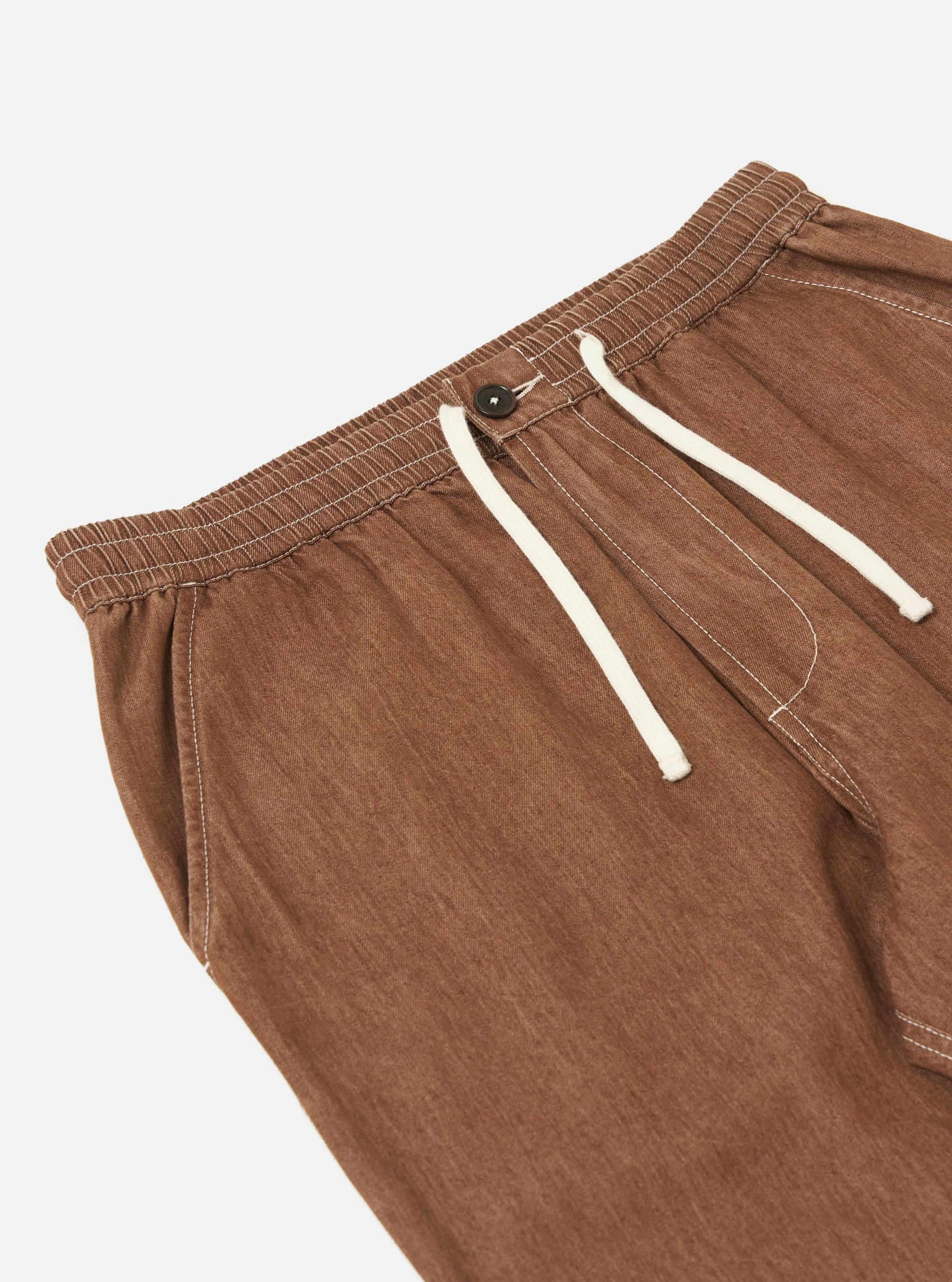 A pair of brown denim hi-water trousers is displayed flat against a plain white background. The trousers feature a slim, cropped leg and an elasticated drawstring waistband.