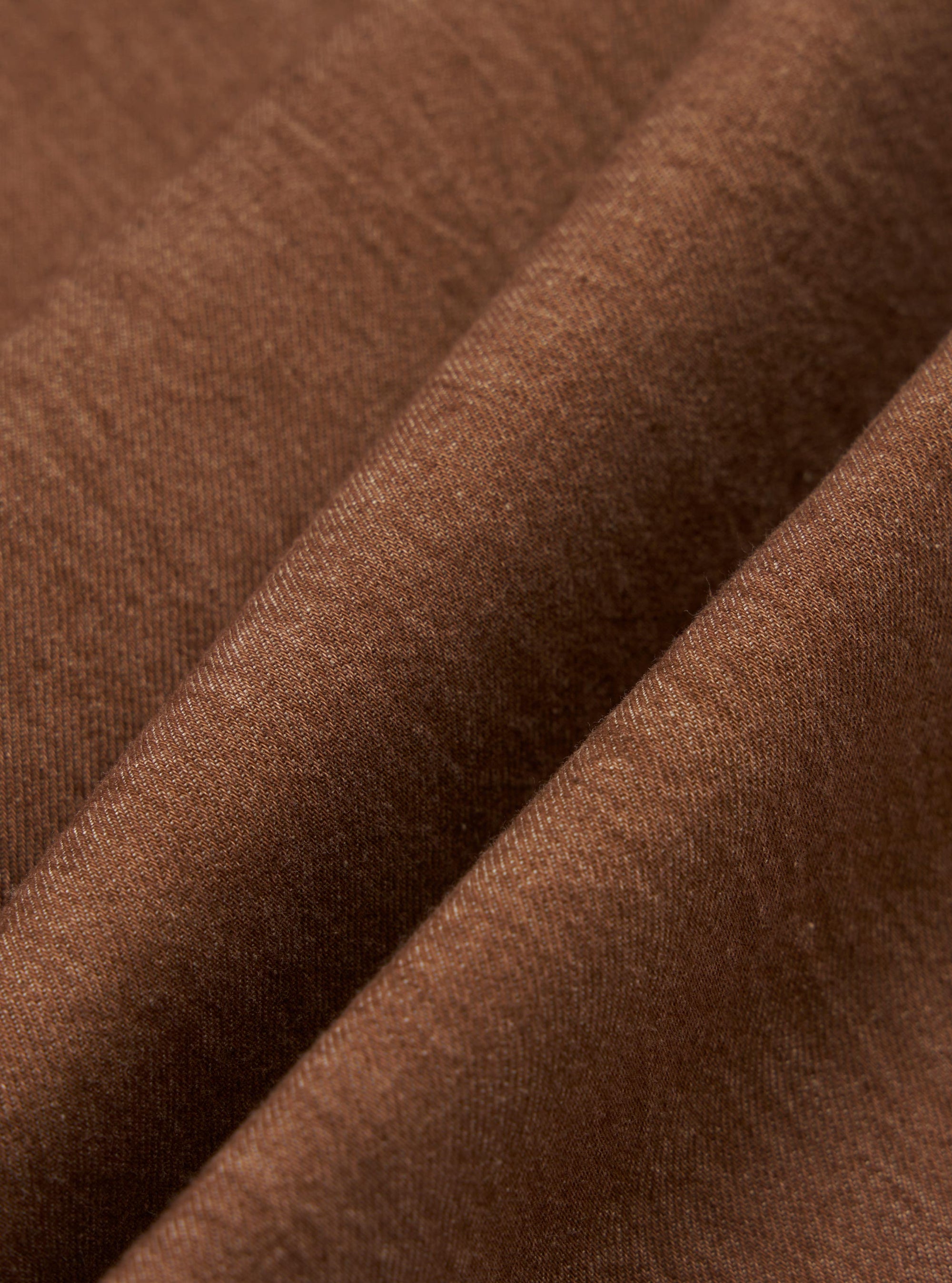 A close-up fabric swatch of the brown Meco denim from the Hi Water Trouser shows a detailed diagonal twill weave. The image captures the texture and earthy brown color of the material.