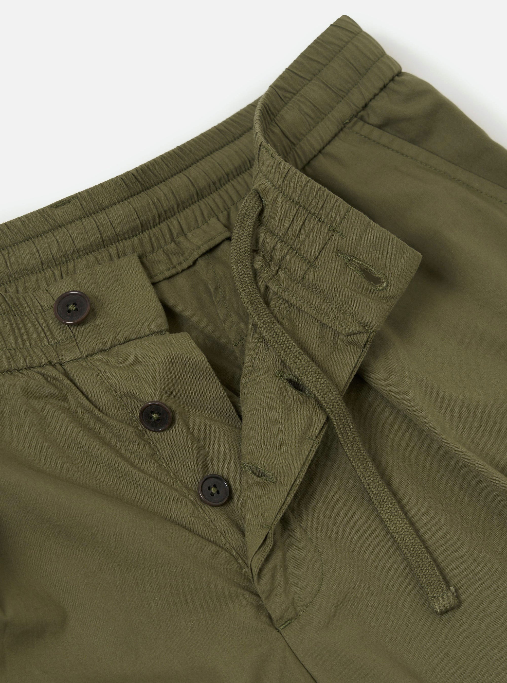 A pair of olive green broadcloth Oxford pants is shown from the back, laid flat against a plain white background. The image highlights the rear construction, including a single buttoned flap pocket on the right side and a clean waistband.