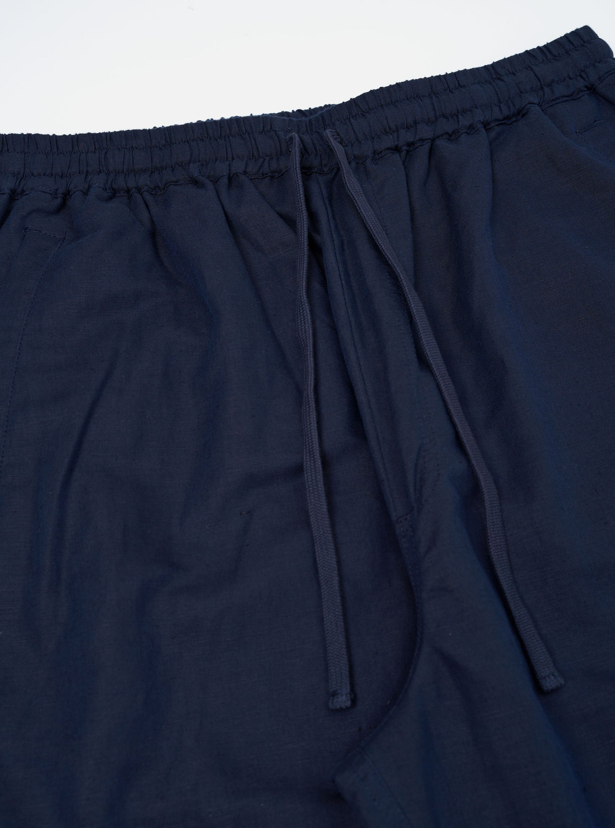 A pair of Navy Linen Cotton Shirting Parachute Pants is shown from the rear, laid flat against a plain white background. The image highlights the two large rear accordion patch pockets with buttoned flaps and the drawstring hem at the ankles.