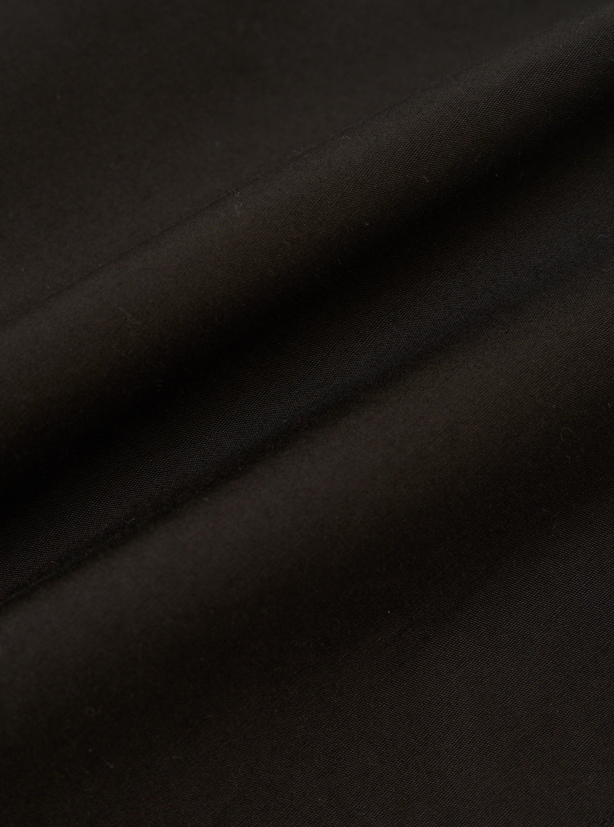 A detailed, close-up fabric swatch of the black cotton broadcloth used for the Vacation Short. The image highlights the fine, tight weave and smooth matte finish of the fabric.