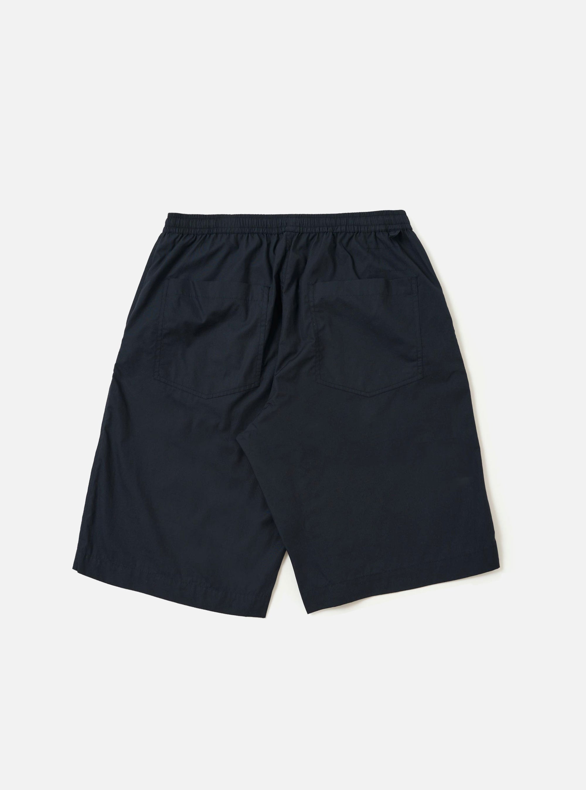 The Navy Broadcloth Vacation Short is shown from a rear angle, laid flat against a plain white background. The image highlights the lightweight navy blue cotton fabric, an elasticated waistband, and a single rear patch pocket on the right side.