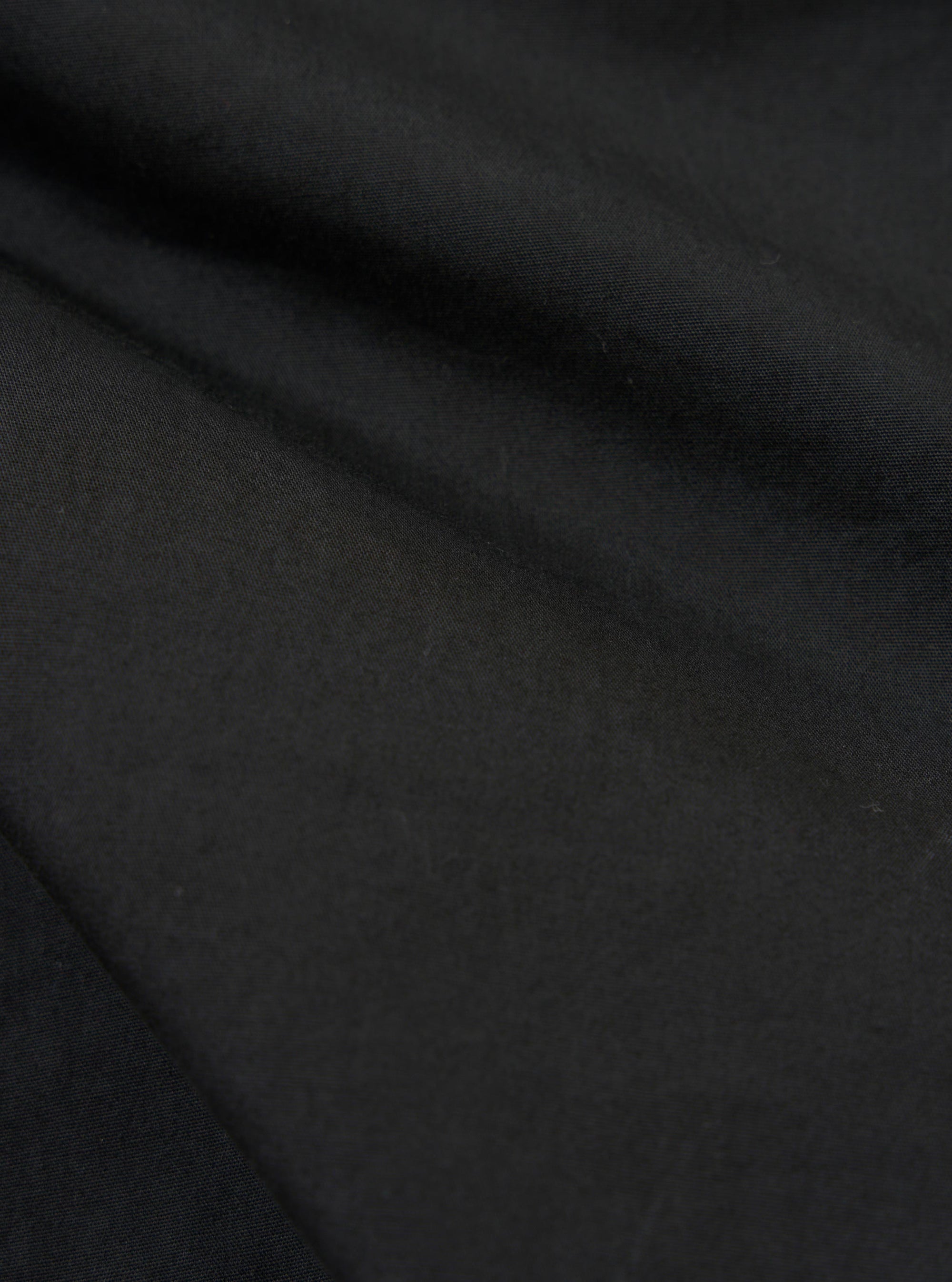 A close-up fabric swatch of the black broadcloth material used for the Camp Shirt. The image displays the tight weave and smooth texture of the solid black fabric.