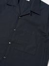 The Navy Broadcloth Camp Shirt is shown from the back, laid flat against a plain white background. The image highlights the back yoke with small pleats and the elongated hem which is longer at the back with side splits.