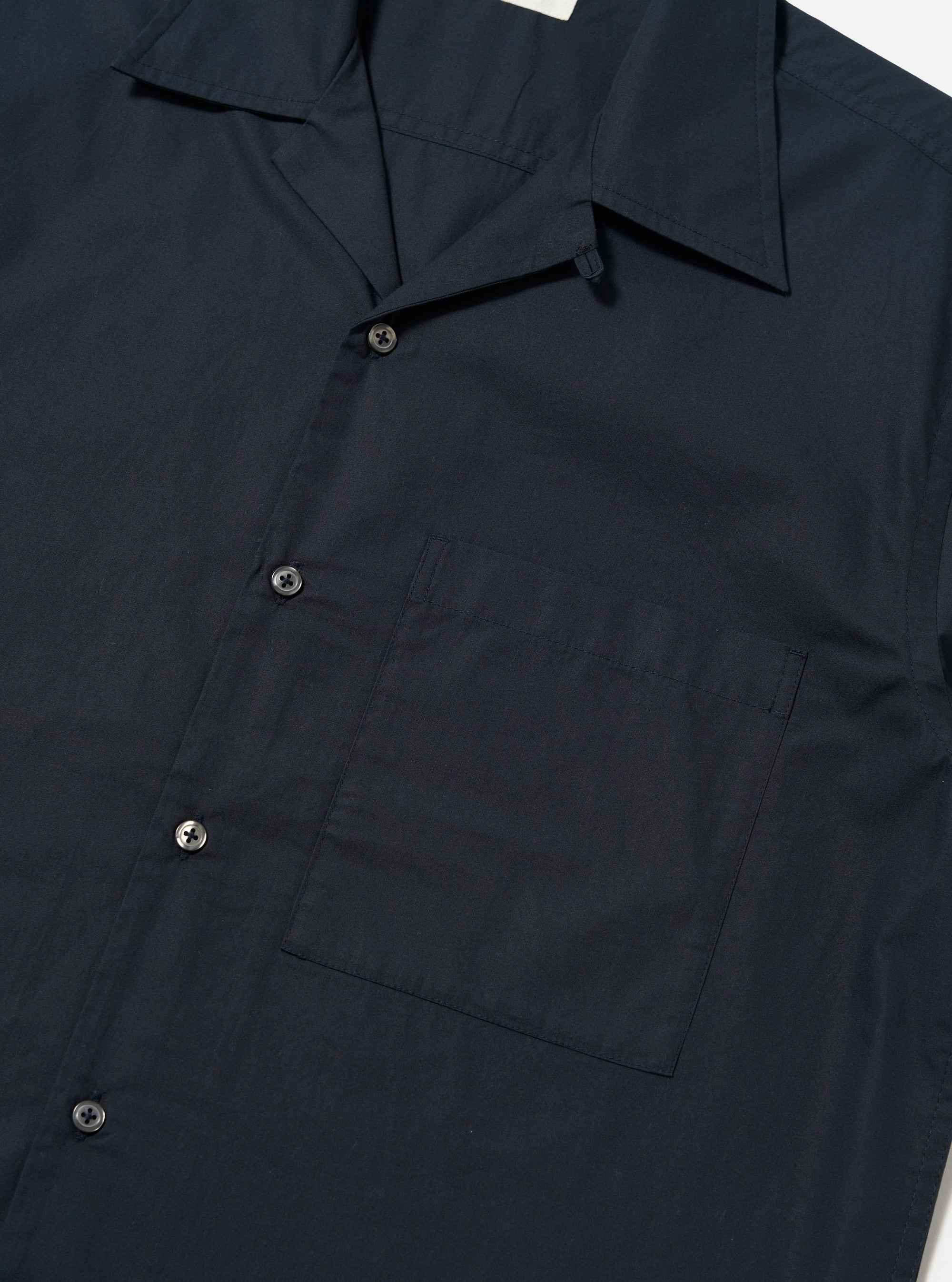 The Navy Broadcloth Camp Shirt is shown from the back, laid flat against a plain white background. The image highlights the back yoke with small pleats and the elongated hem which is longer at the back with side splits.