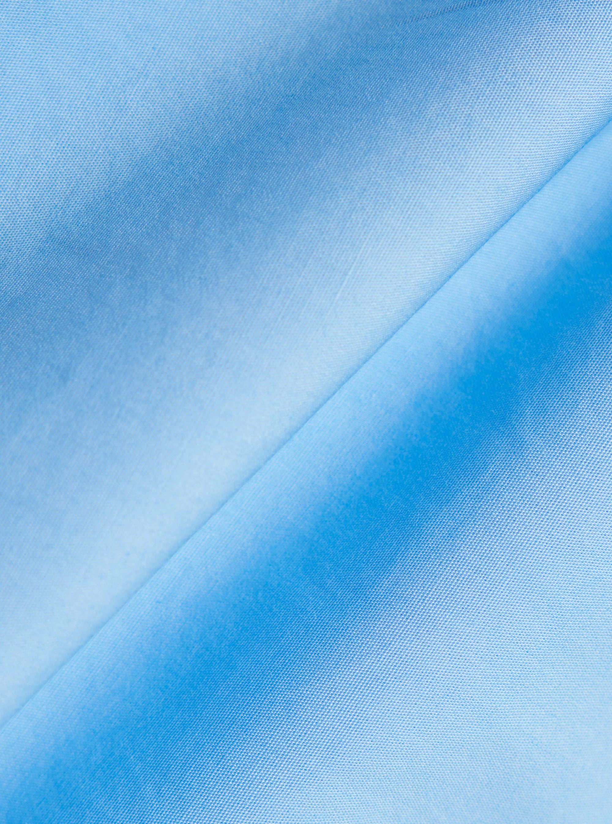 A detailed close-up fabric swatch of the Pale Blue Broadcloth Lucky Shirt shows the fine, smooth texture of the solid pale blue cotton broadcloth. The image focuses on the uniform, dense weave of the material.