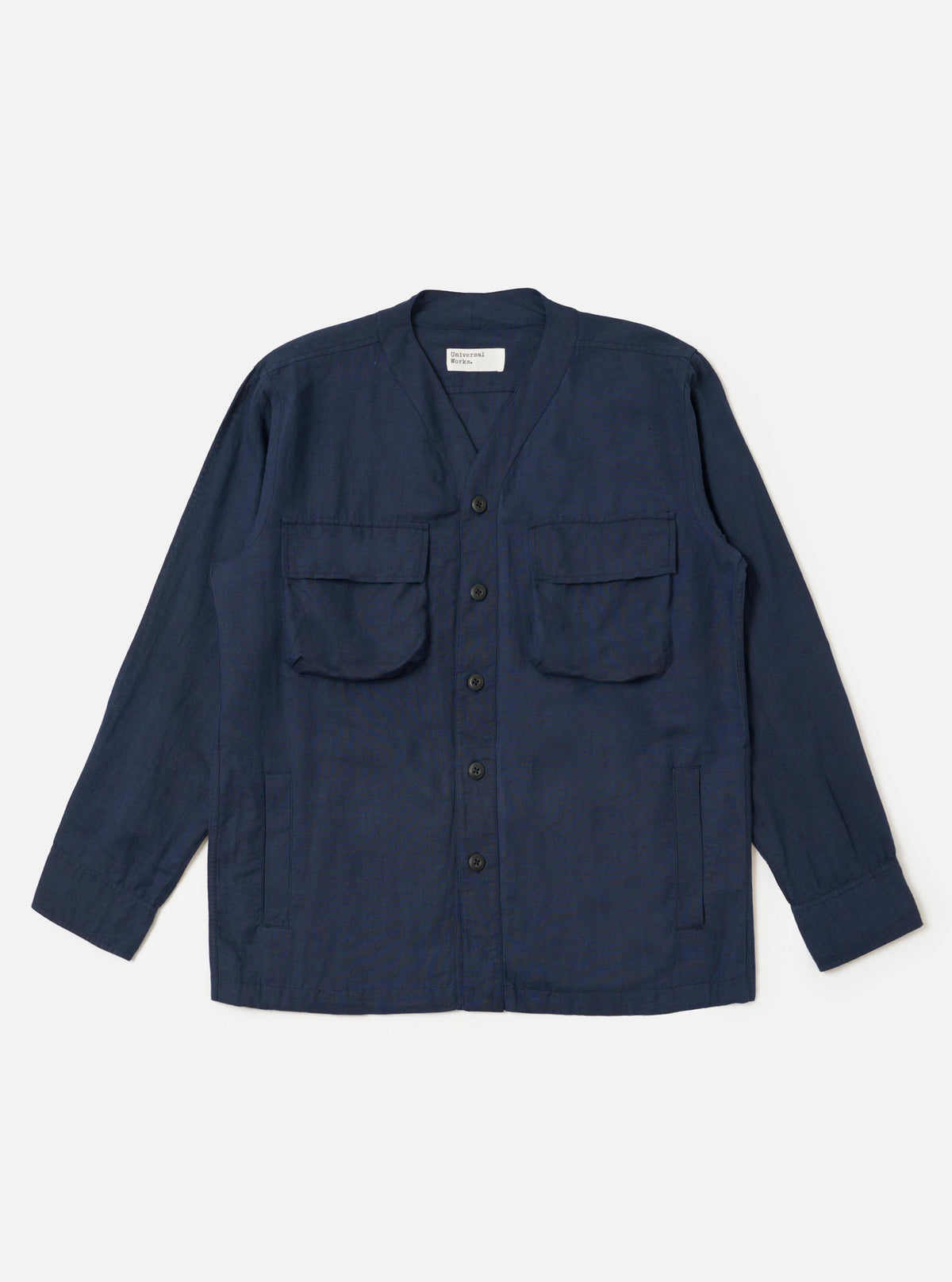The Navy Linen Cotton Shirting Parachute Shirt is shown laid flat against a solid white background. The garment features a collarless V-neckline with a cardigan-style button front, two large 3D bellows pockets on the chest with buttoned flaps, and two vertical welt hand pockets near the hem. The shirt has long sleeves with adjustable button cuffs and a straight hem with an internal drawcord.