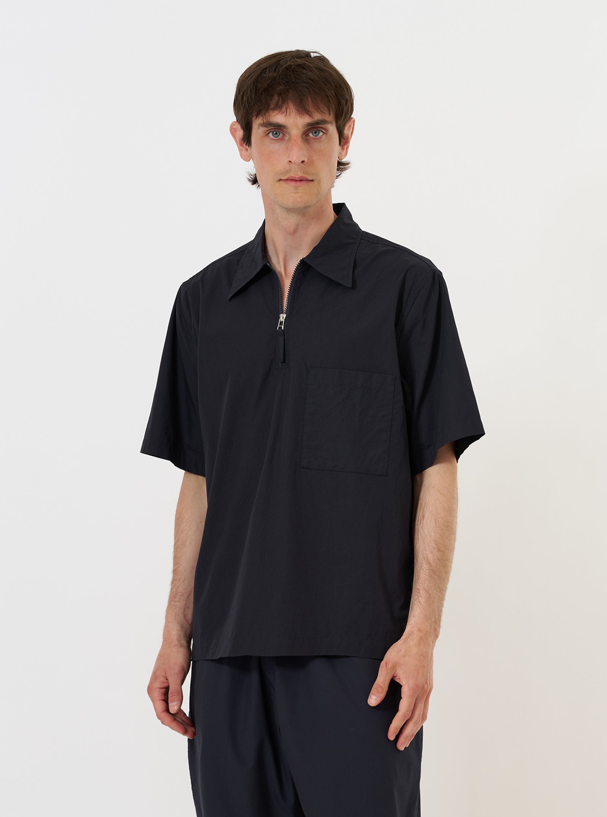 A model is wearing the Navy Broadcloth Ewan Shirt against a plain white background. The shirt is a navy blue pullover style featuring a partial zip front, a classic collar, and a single chest pocket. The model is shown from the waist up, and the garment is worn untucked. No mannequin is present in the image.