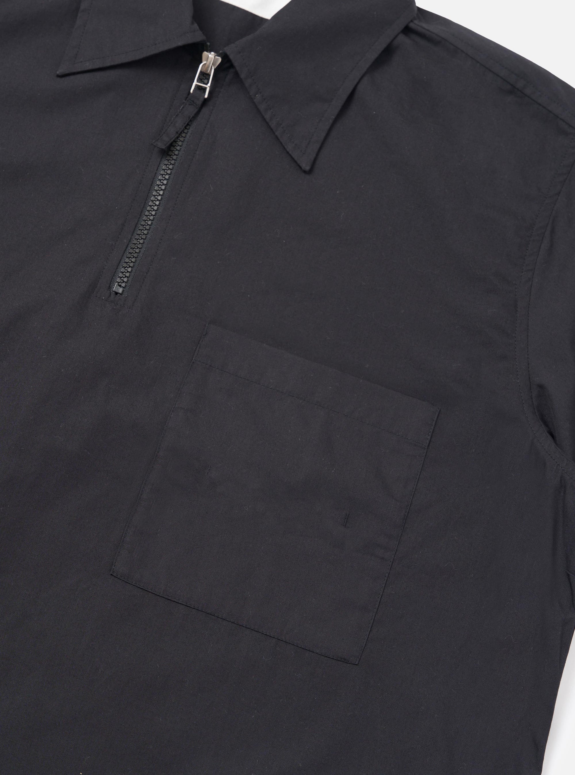 The back of the Black Broadcloth Ewan Shirt is shown laid flat against a plain white background. The image highlights the clean construction and smooth texture of the black cotton broadcloth fabric, featuring short sleeves and a straight hem.
