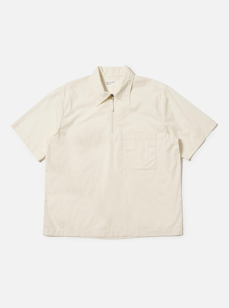 The Ecru Broadcloth Ewan Shirt is shown laid flat against a plain white background. This pullover-style shirt features a classic pointed collar, a short zip-front placket, and two large chest pockets. The long sleeves are positioned at the sides, and the garment is made from a smooth, ecru-colored cotton broadcloth.