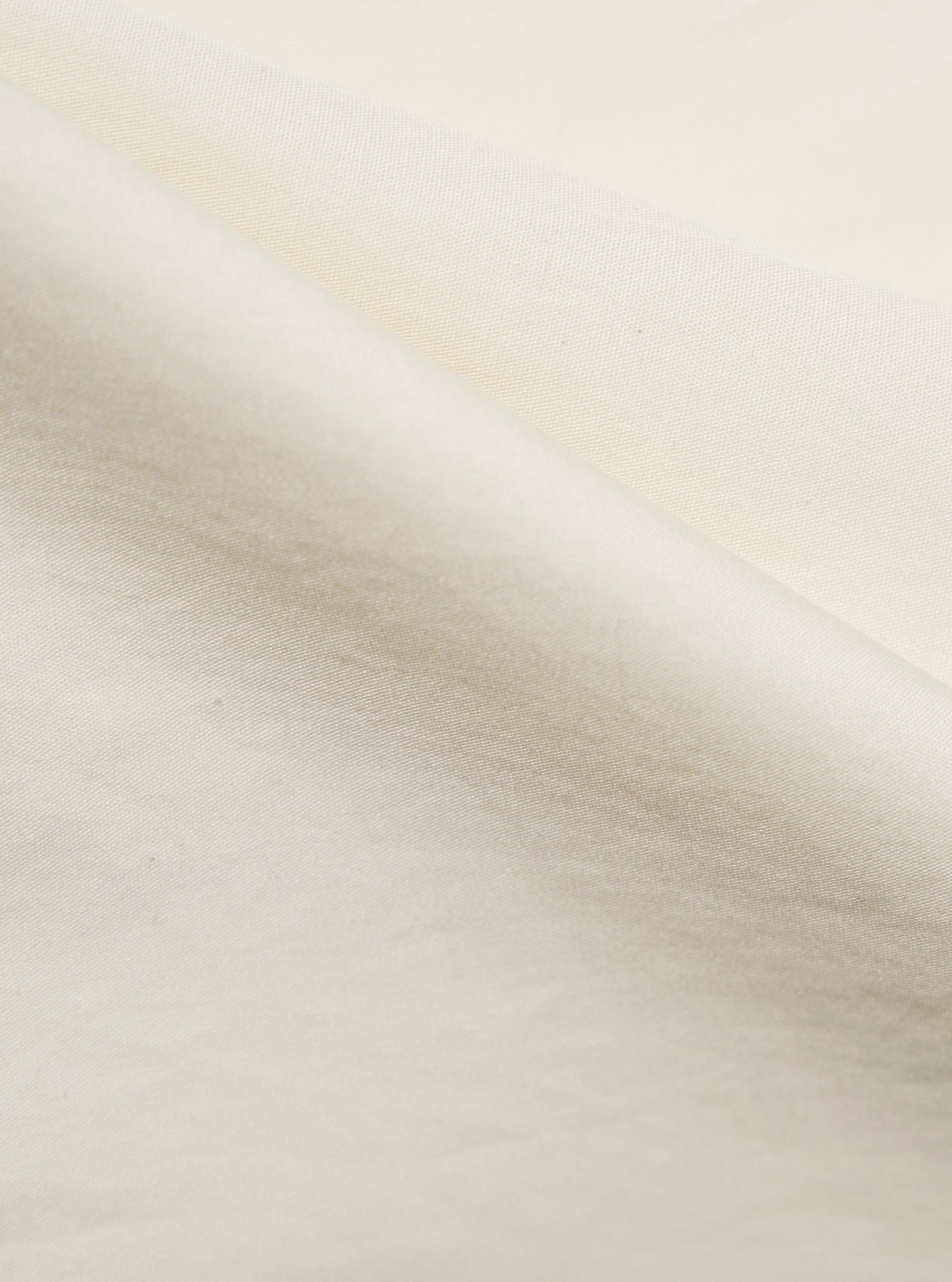 A close-up fabric swatch of the Ecru Broadcloth Ewan Shirt shows a detailed view of the fine, plain-weave cotton fabric. The image highlights the smooth texture and off-white ecru color of the material.