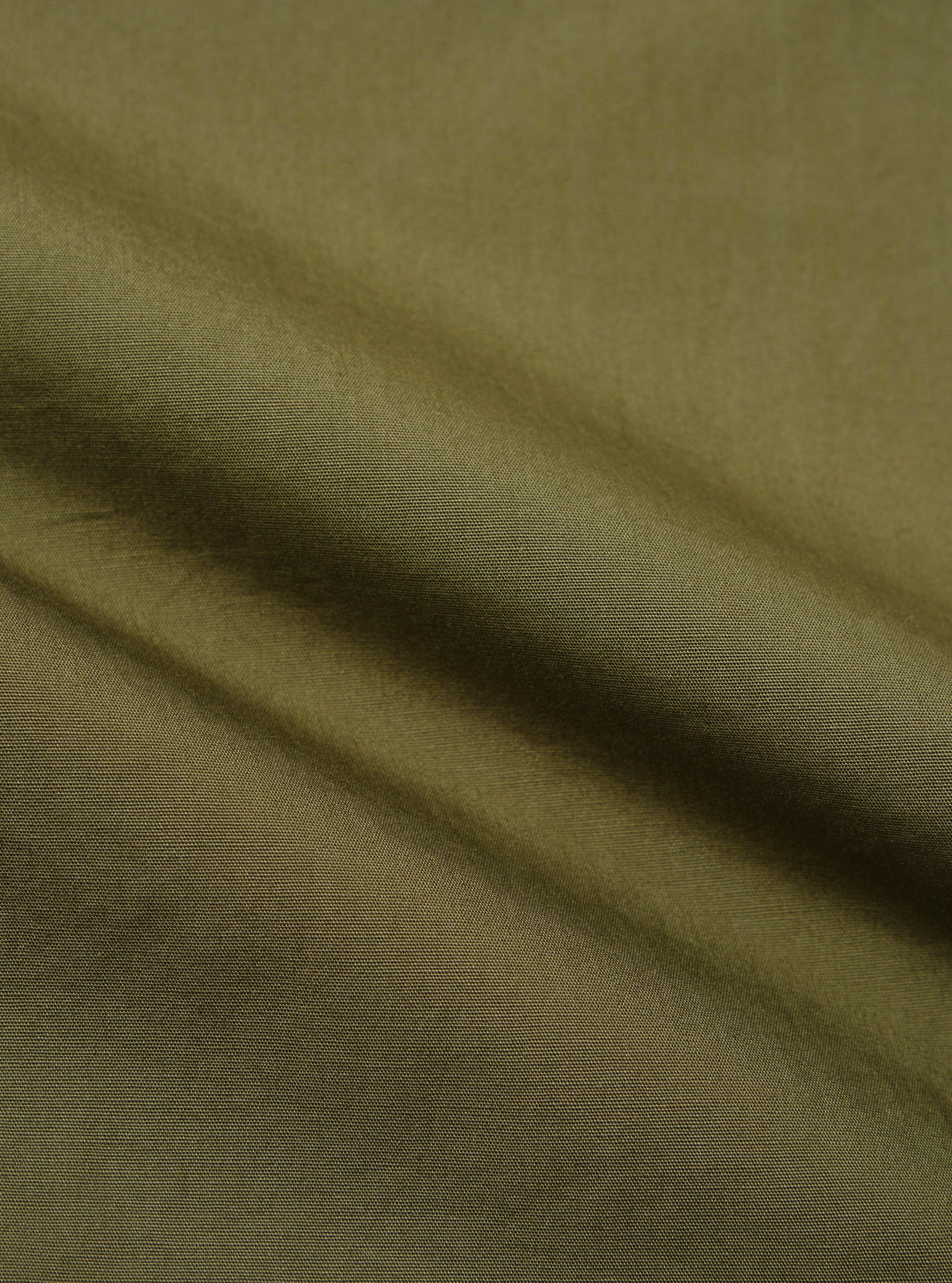 A close-up fabric swatch of the olive green broadcloth used for the Ewan Shirt. The image displays the smooth, tight weave and solid olive color of the material.