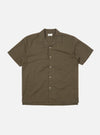 An Olive Linen Cotton Shirting Camp Shirt is displayed flat against a plain white background. The shirt features a relaxed fit with a one-piece camp collar, a full button-down front, and a single large patch pocket on the left chest. The short-sleeved garment is shown in a muted olive green color with a visible textured slub weave.
