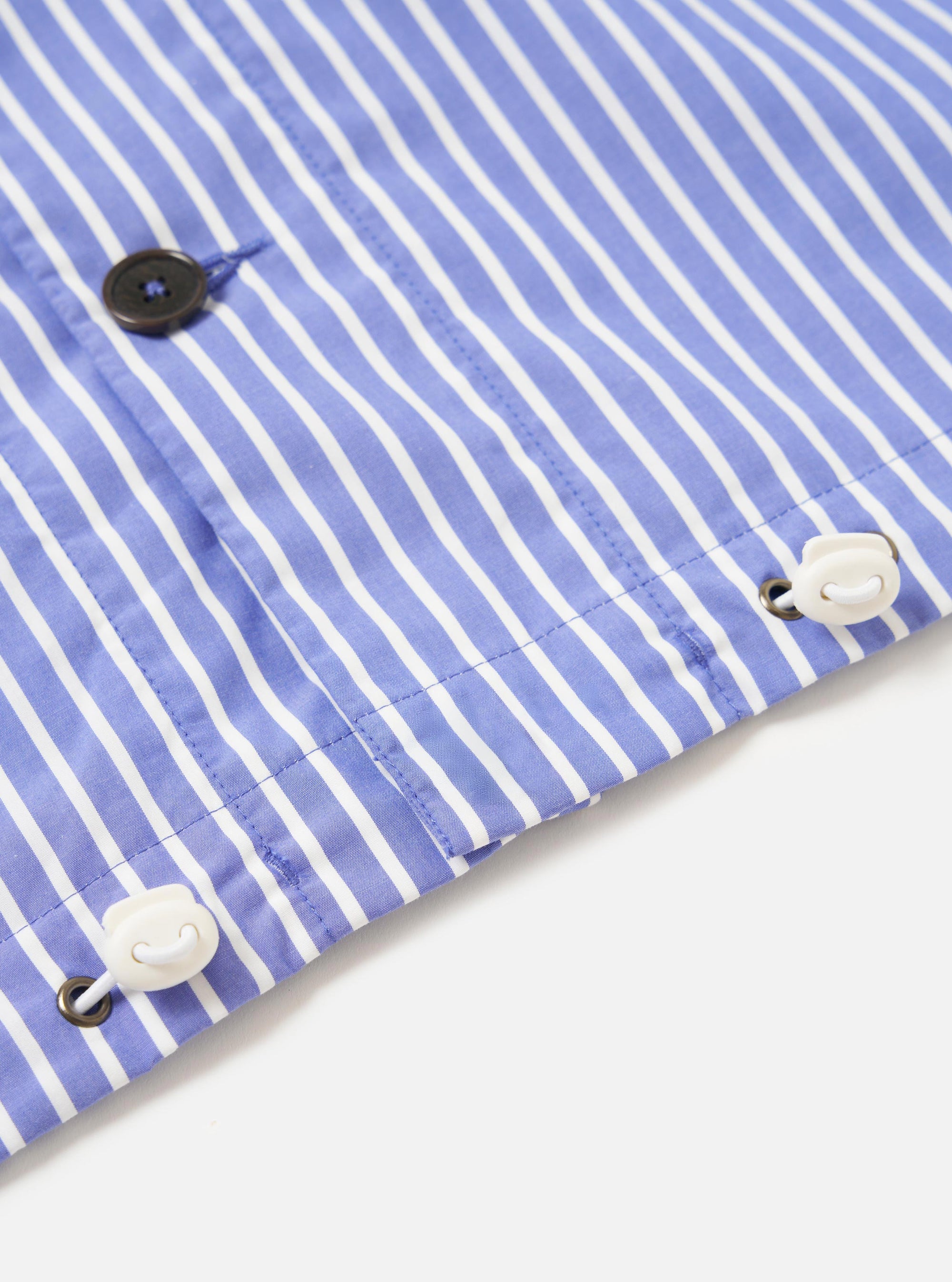The Blue/White Cotton Stripe Z Tech Overshirt is displayed from the back, laid flat against a plain white background. The image highlights the horizontal back yoke and a central box pleat, showcasing the fine blue and white vertical stripe pattern of the cotton fabric. The elasticated hem is prominent at the bottom of the garment.