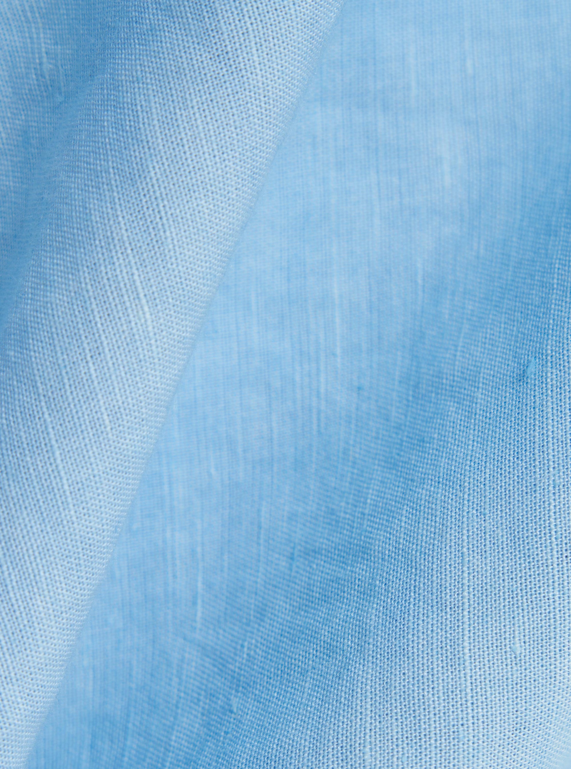 A detailed, close-up fabric swatch of the Pale Blue Linen Cotton Shirting Bakers Overshirt shows the textured weave of the light blue material. The image highlights the natural slub and grain of the linen-cotton blend against a neutral, blurred background.