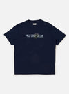 The Navy Single Jersey Trail Trail To Hotel Delux Tee is shown laid flat against a solid white background. The navy blue short-sleeved T-shirt features a classic crew neck and a prominent graphic print on the chest consisting of white text and a circular emblem.