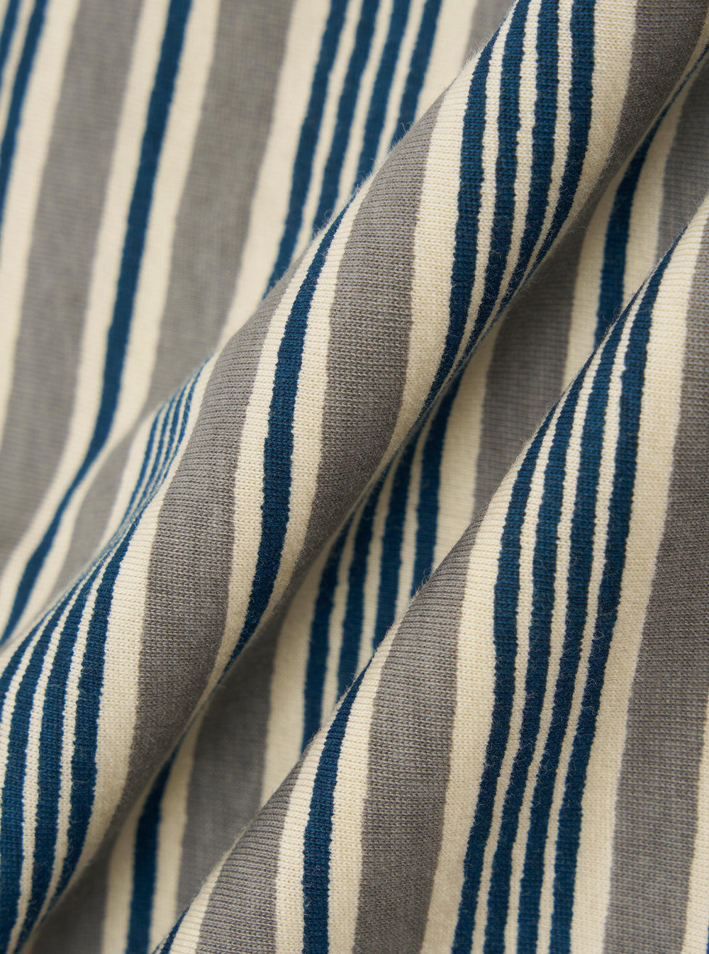A square fabric swatch of the Grey OS Stripe Jersey Core Tee features a detailed close-up of a pale grey and white horizontal striped pattern. The fabric has a soft, irregular character with a lightweight jersey texture.