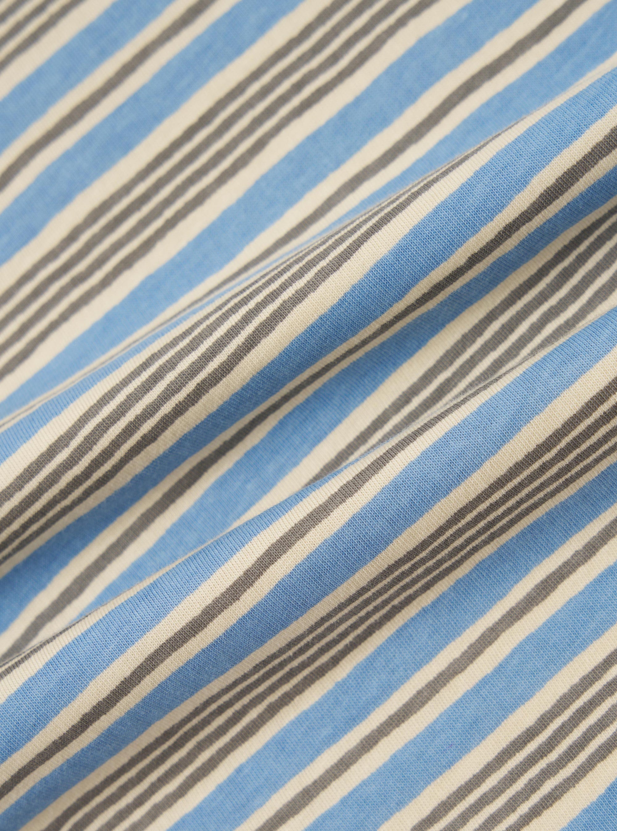 A close-up, square fabric swatch of the Pale Blue OS Stripe Jersey Vacation Polo highlights a detailed pattern of very thin, horizontal light blue and white stripes. The image focuses on the texture of the soft jersey cotton material.