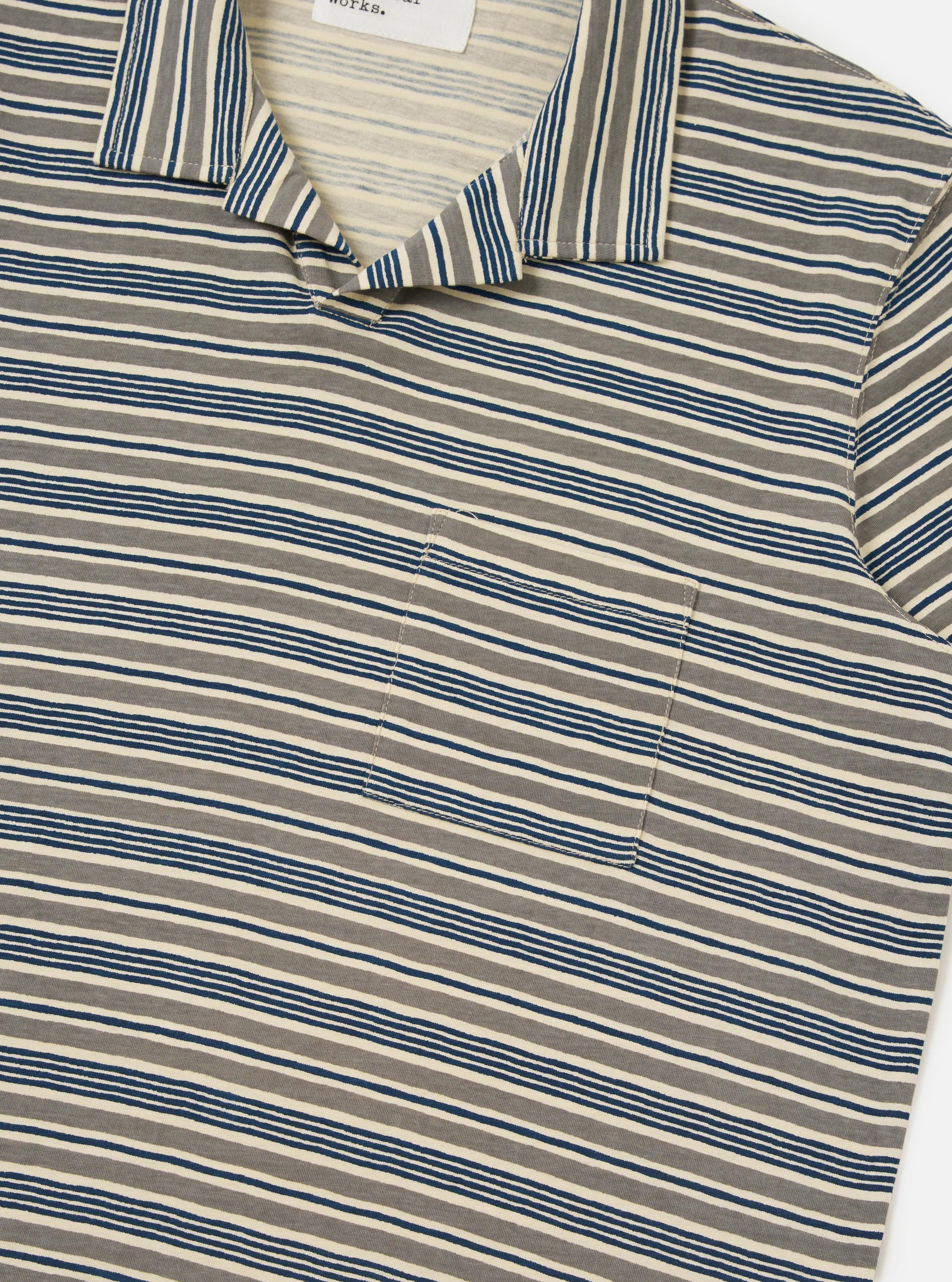 A model is seen from a rear perspective wearing the Grey OS Stripe Jersey Vacation Polo against a plain white background. The image highlights the shirt's relaxed fit, the horizontal grey and white brush-drawn stripes, and the stepped hem which is slightly longer at the back. No mannequin is present in the image.