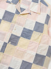 The Pastel Check Patchwork Camp Shirt is shown from the back, highlighting the construction of various multicolored plaid panels. The shirt features a horizontal back yoke with two small pleats and a straight hem with side splits. The garment is laid flat against a plain white background, and