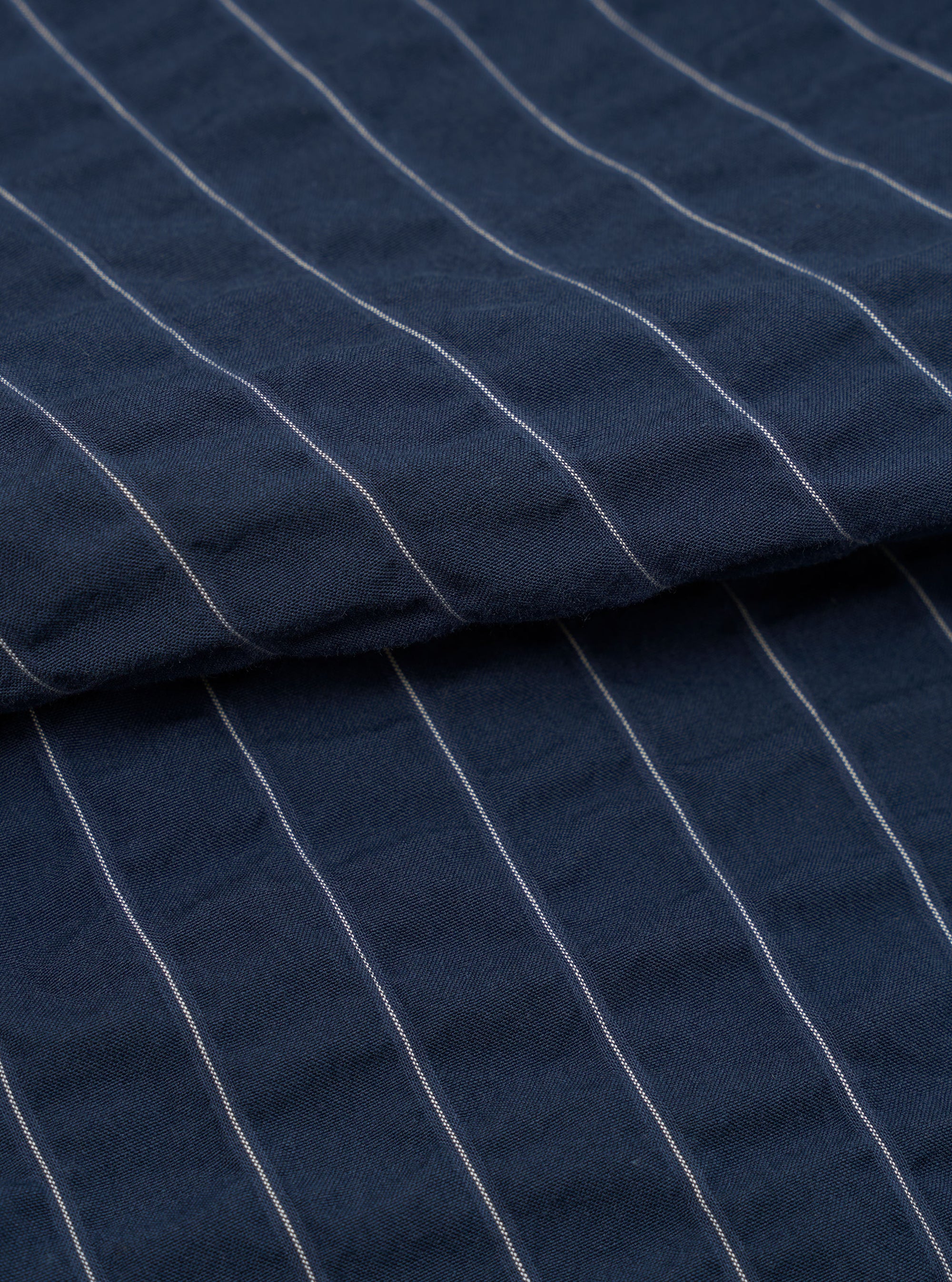 A close-up fabric swatch of the Navy Chester Stripe Oxford Pant is shown against a plain white background. The image highlights the fine vertical pinstripe pattern on the navy blue cotton fabric, showcasing the material's texture and detail.