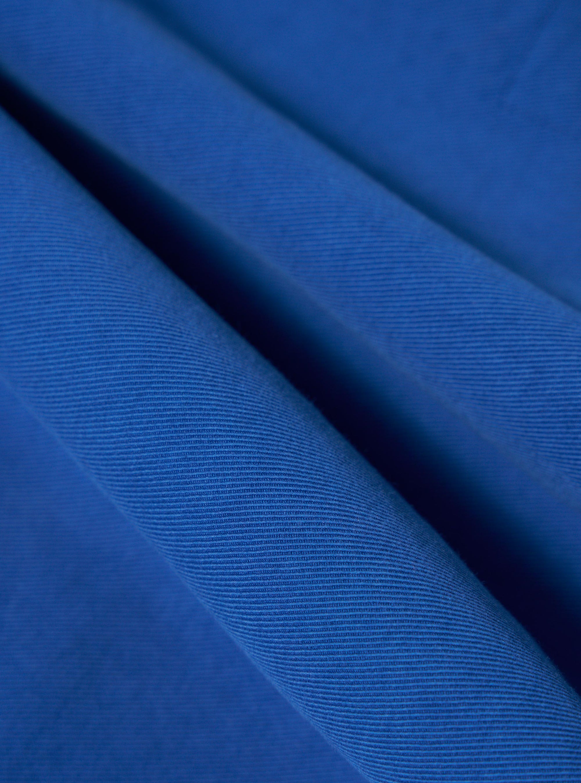 Close-up of the Paraboot x Universal Works Navy Derek Twill Warmus Jacket fabric. The twill weave is visible in a vibrant navy blue.